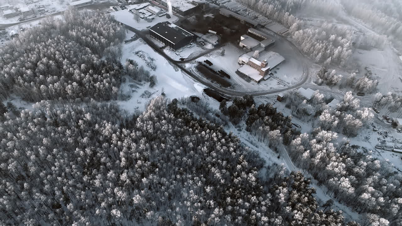 눈 덮인 소나무 숲 뒤에 드러난 김이 나는 공장의 항공 샷