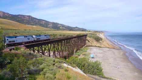 aerial shot of an amtrak passenger train traveling south along the coast of central california and over the gaviota trestle