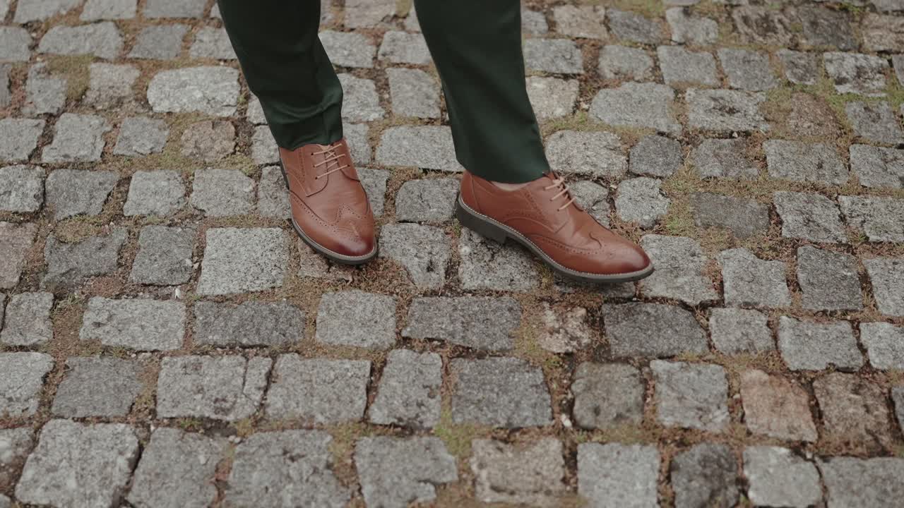 close up of groom's legs walking on cobblestone pavement wearing brown formal shoes