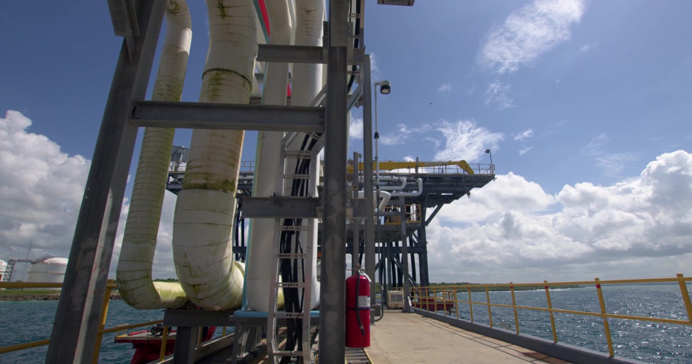 Tilt down shot starting from steel pipeline rack under bright sunlight down to the pier walkway and offshore unloading platform at Coastal Petroleum terminal in San Pedro de Macoris, Dominican Republi