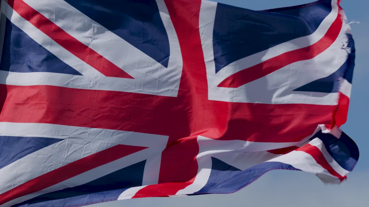 Union Jack flag flutters dynamically against blue sky, bright daylight, close-up, steady camera