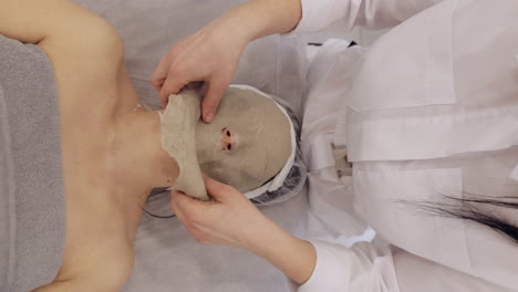 beautician applying medical peeling face mask on middleaged woman skin care procedure in spa salon