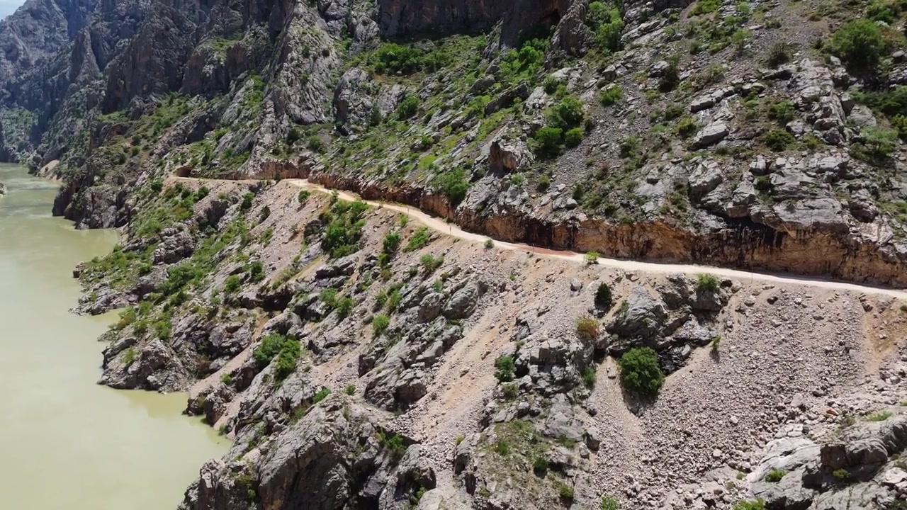 Toma de dron siguiendo el curso del río Karasu con la legendaria Carretera de Piedra tallada a mano visible en el acantilado con un túnel excavado en la roca en el cañón de Kemaliye, Turquía