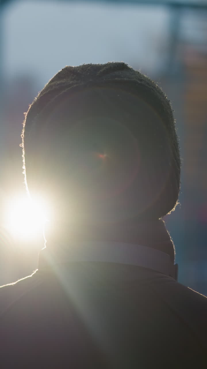 vista trasera de una persona con un traje negro y gorra, levantando una pelota con un auricular alrededor de su cuello, el fondo presenta un borrón de luces de la ciudad y un brillo reflectante en la distancia