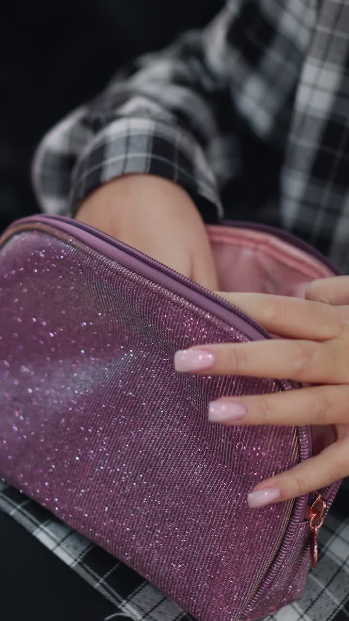 borsetta viola scintillante e mani di donna che ne esplorano il contenuto, primo piano di dita curate che aprono una pochette glitterata appoggiata sulle gambe, la camicia a quadri suggerisce una scena urbana casual con una delicata luce naturale, dettagliata