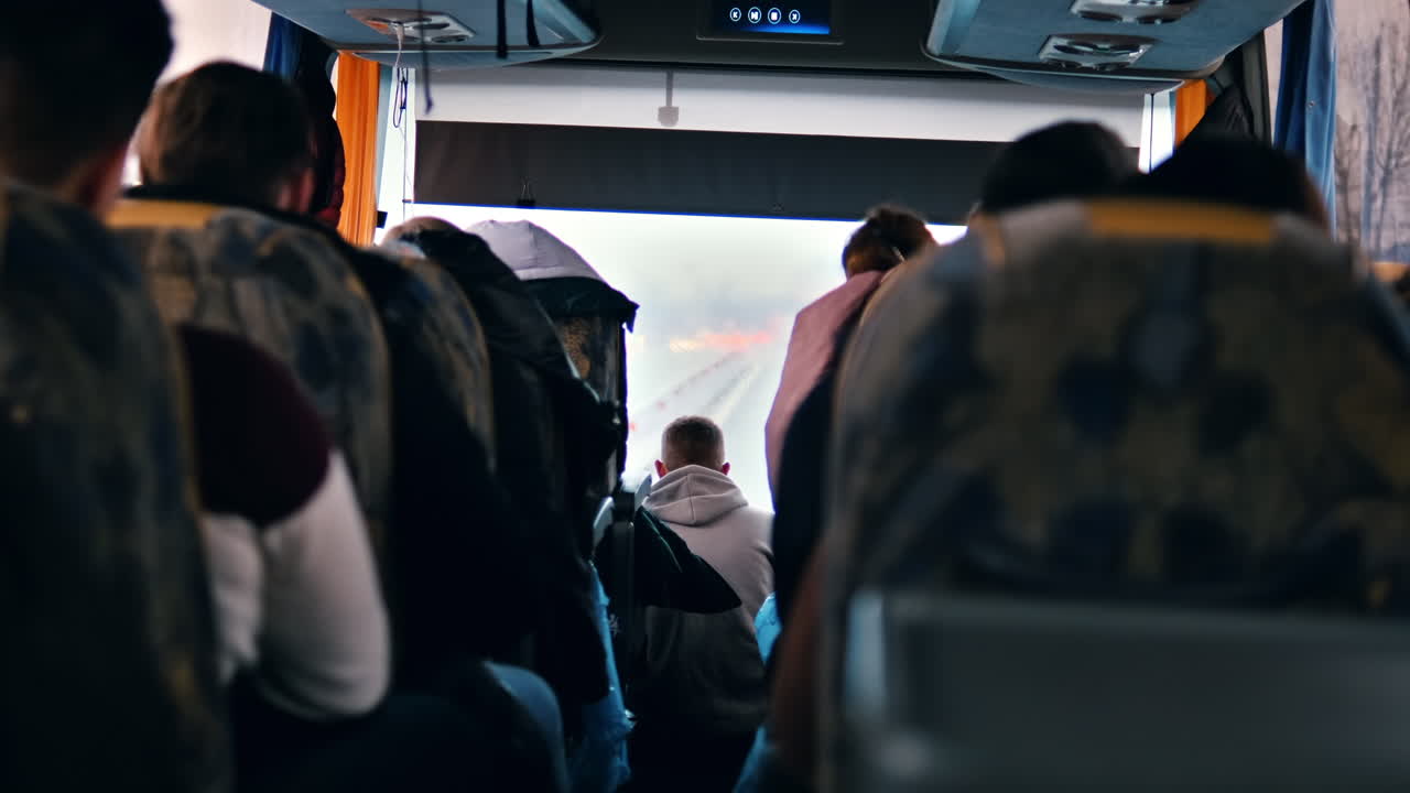 View of interior of a bus, multiple sitting people, road visible through the window