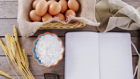 libro, huevos, harina, cortador de galletas y tallo de trigo mantenido en una mesa 4k