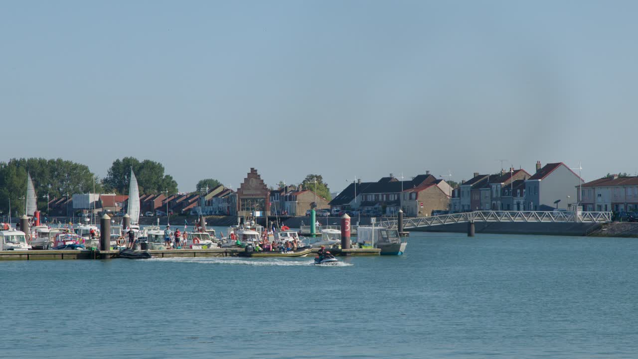 Jet ski moves across calm marina waters with boats, waterfront buildings, and clear daylight