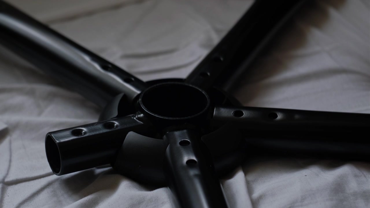 Close-up estático de mãos posicionando uma estrutura de base de cadeira de metal em uma superfície de tecido durante a montagem de móveis internos