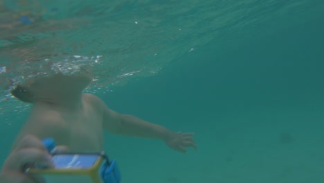 niño con cámara en caja impermeable bañándose en el mar