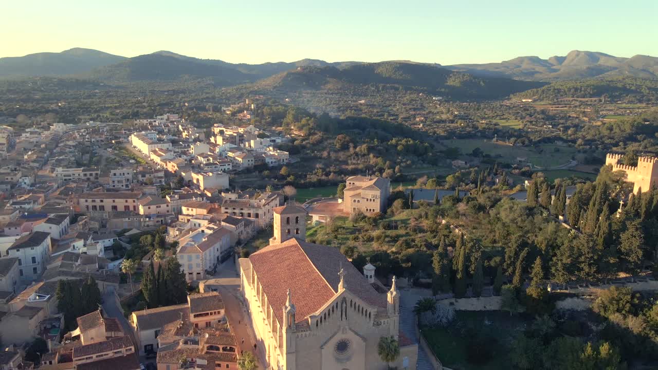 Experience the breathtaking panoramic view of Arta in Mallorca as the sun sets, casting warm hues over the town and surrounding hills.