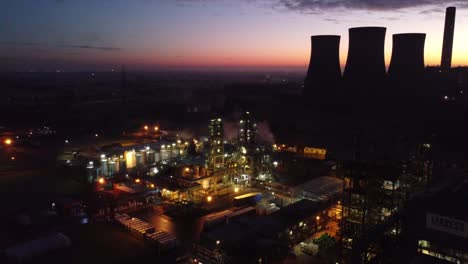 illuminated aerial night view above industrial pipeline chemical factory site pull away right
