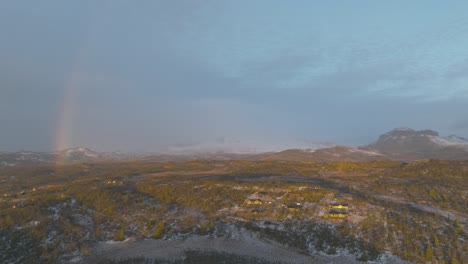 Regenbogen-Und-Sonnenaufgang-über-Einigen-Hütten-In-Den-Norwegischen-Bergen-Mit-Etwas-Schnee-Im-Hintergrund