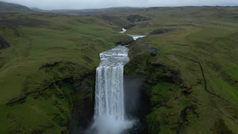 Vista-Aérea-Desde-La-Cascada-De-Skogafoss-Con-Una-Caída-De-60-M-Rodeada-Por-Un-Increíble-Paisaje-Verde-En-El-Sur-De-Islandia-Durante-El-Verano.