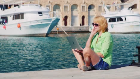 chica turista usa una laptop en el fondo del paisaje urbano con yates