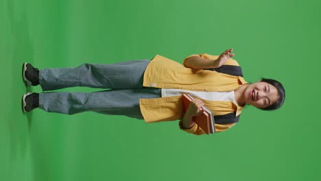 full body of asian woman student with a backpack holding some books and saying wow while standing in the green screen background studio