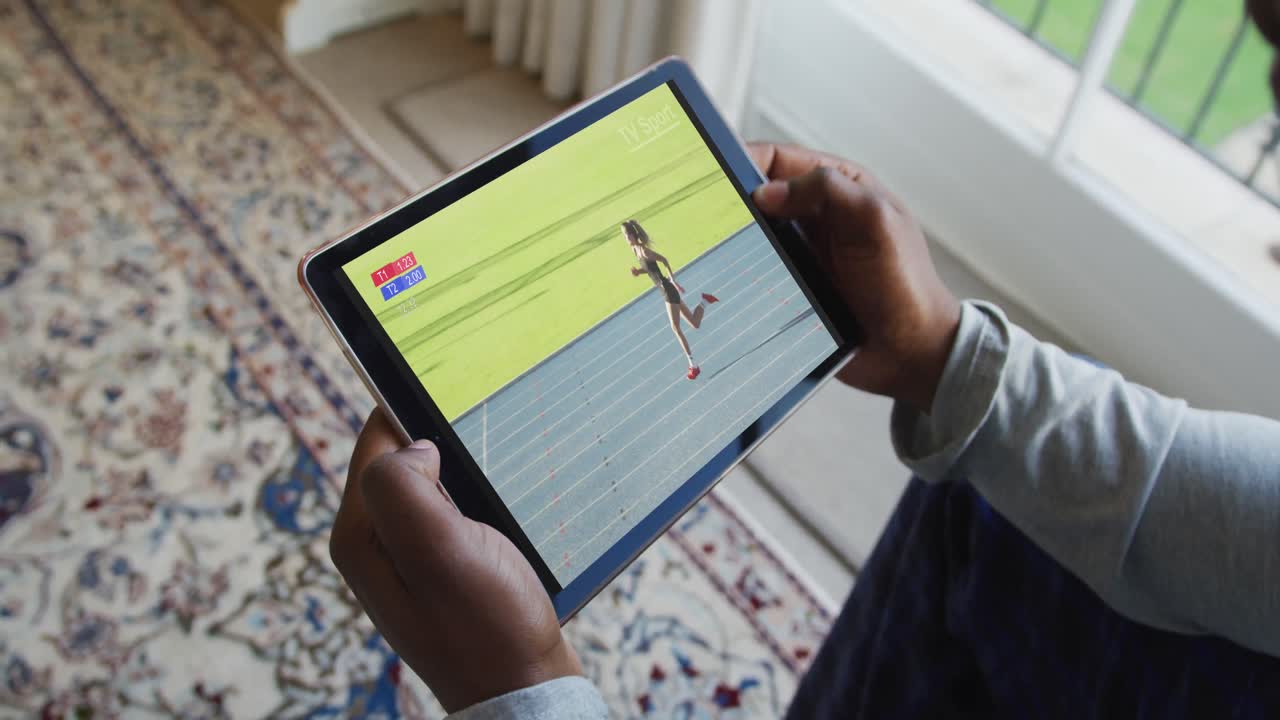 Composite of man sitting at home, watching athletics running event on tablet