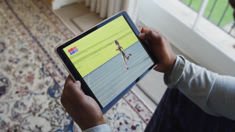 compuesto de un hombre sentado en casa, viendo atletismo corriendo evento en la tableta