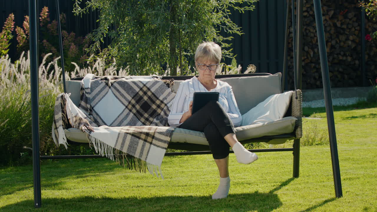 Portrait of senior woman using a tablet. Sitting in a garden swing in the backyard of a house