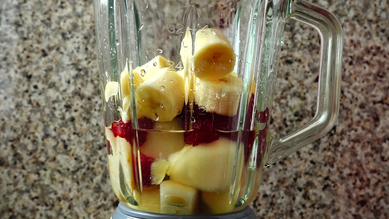 Riempire il frullatore con pezzi di pera, lamponi e banane. Preparazione del frullato nel frullatore.