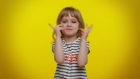 una niña pequeña sonríe y juega con sus manos mientras lleva una camisa a rayas con un corazón en ella
