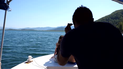 young pair sitting on bow of boat and posing to unrecognizable photographer. happy couple in love spending time together on deck of ship and enjoying summer travel. concept of vacation or holiday.