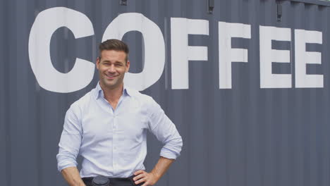 Portrait-Of-Male-Owner-Of-Coffee-Shop-Or-Distribution-Business-Standing-By-Shipping-Container