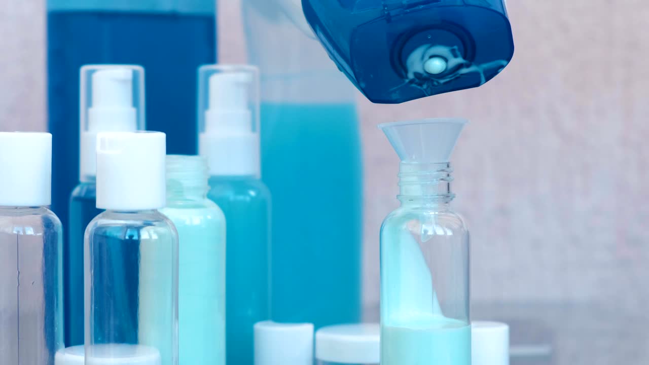 Woman's hands pour blue shampoo in a small bottle of big through a funnel. Travel set of jars. Bottle close-up.