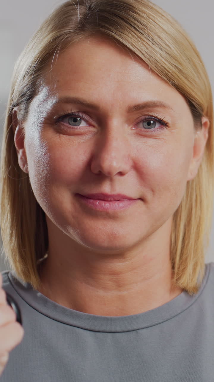 Primer plano de una mujer con unas tijeras cerca de la cara, con una sonrisa sutil y una expresión serena; ambiente de salón con iluminación suave y fondos neutros donde se ve a la estilista preparándose para cortar el pelo y a la clienta eligiendo un nuevo look, creador