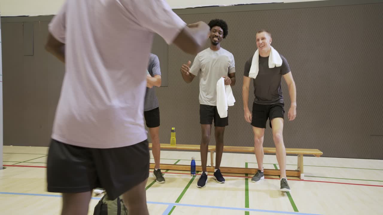 Et forskelligt mandligt hold hører en stående spiller hilse på nytilkomne og række håndklæde og bold i fitnesscenteret.