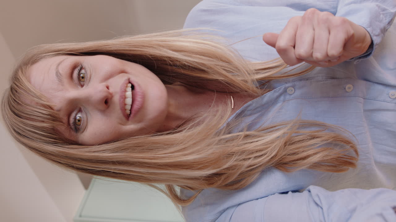 아름다운 여성이 집에서 스마트폰을 사용하여 비디오 채팅을 하고 아파트 채팅을 과시하고 흥미진진한 라이프 스타일을 공유하고 수직 화면에서 온라인 커뮤니케이션을 즐기고 있습니다.