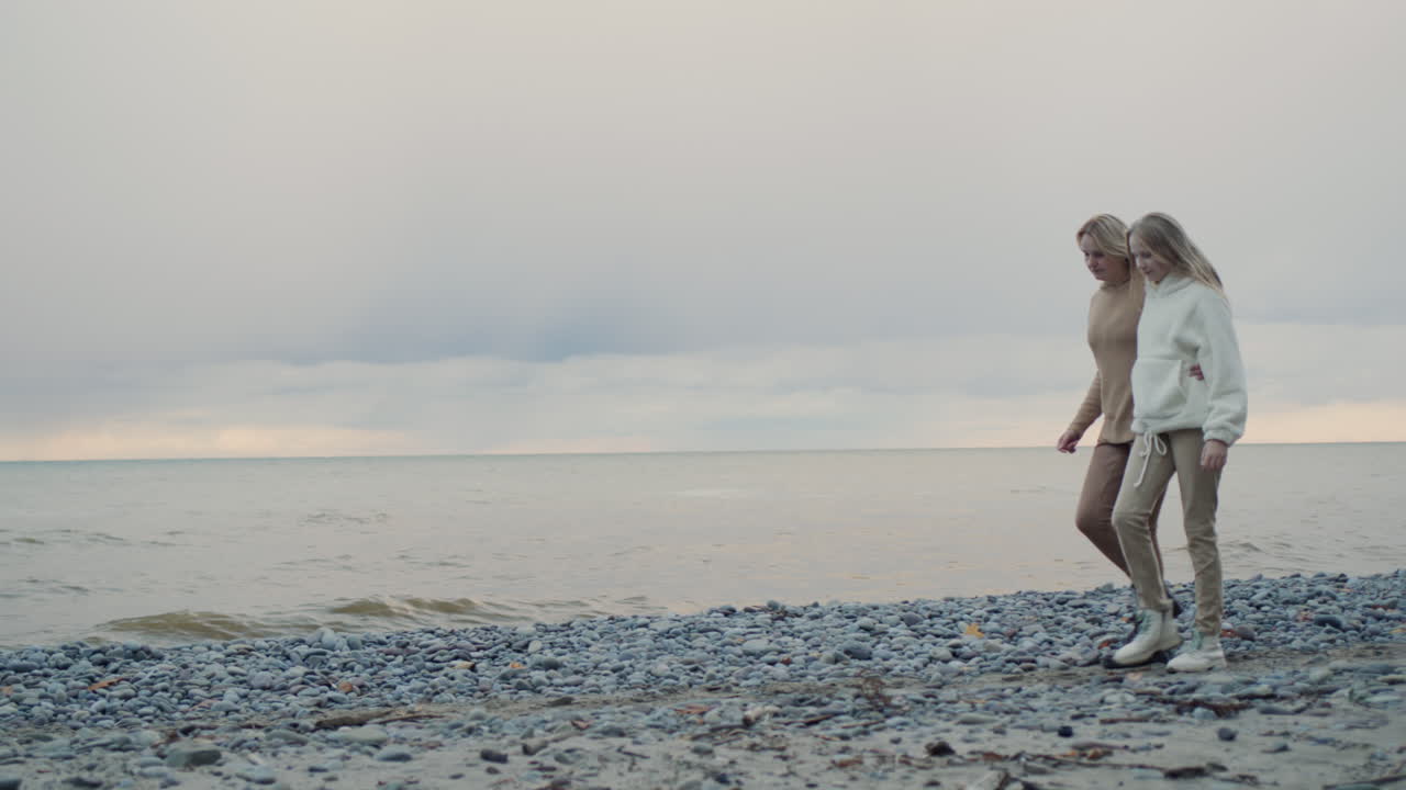 딸 과 함께 있는 한 여자 가 폭풍 하늘 을 배경 으로 해변 을 따라  ⁇ 고 있다