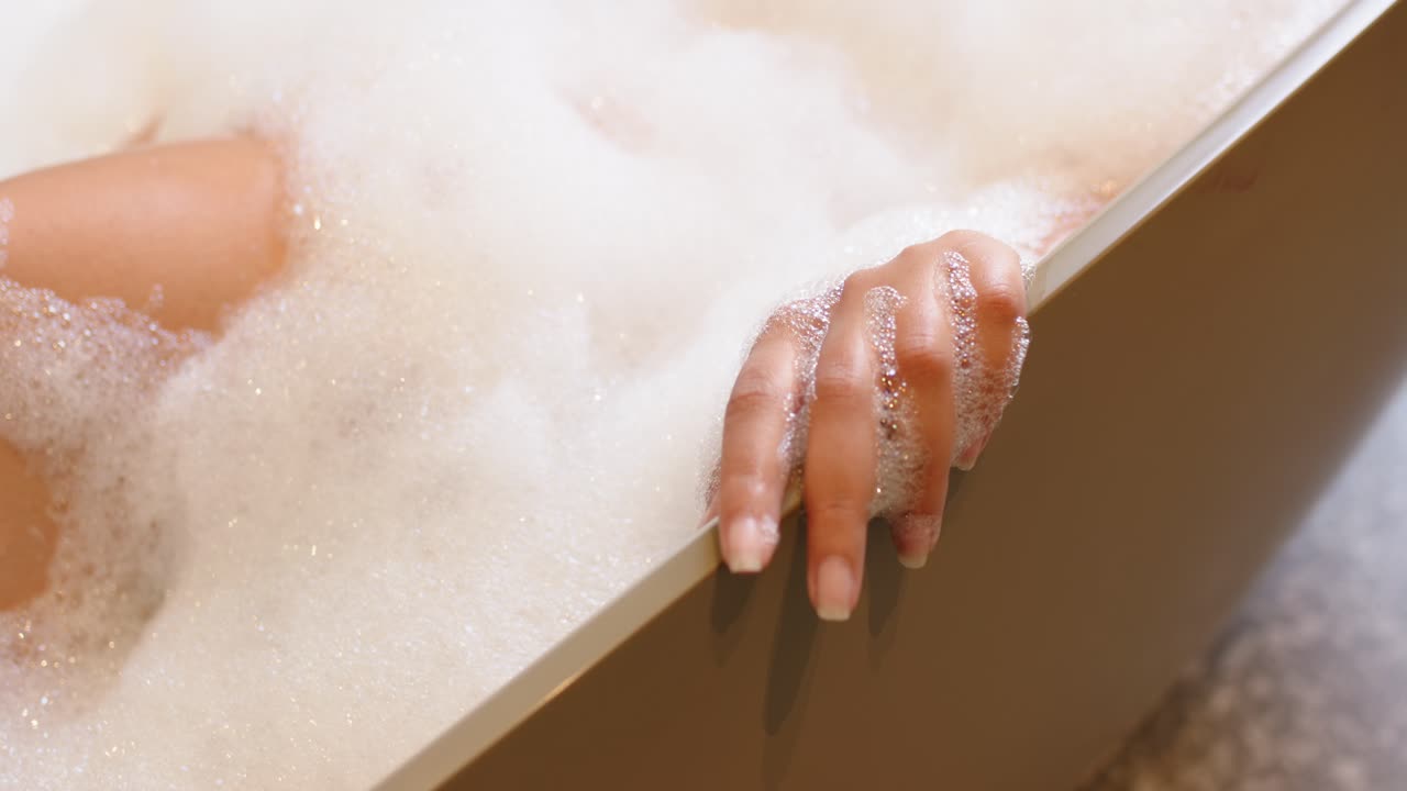 Donna afroamericana adulta che fa scivolare la mano sul bordo della vasca con la schiuma che si muove, rilassandosi, spazio per il testo