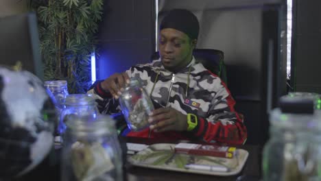 a black man inspects a mason jar filled with marijuana then opens it to smell the aroma of the pot