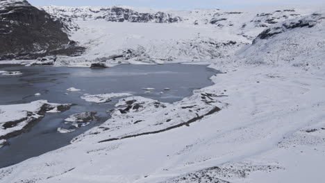 aerial rotating shot of a frozen lake within an icelandic mountain valley