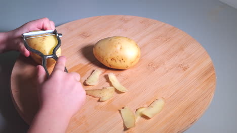 Hands-of-little-girl-peeling-potatoes-with-peeler-on-wooden-desk,-childhood-and-domestic-help-concept