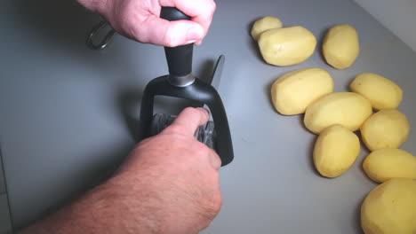 cámara lenta de las manos del hombre afilando un cuchillo de cocina en un afilador, patatas peladas en la parte superior de la cocina