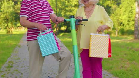 una pareja elegante de mayores abuela, abuelo después de comprar con bolsas usando scooter para montar