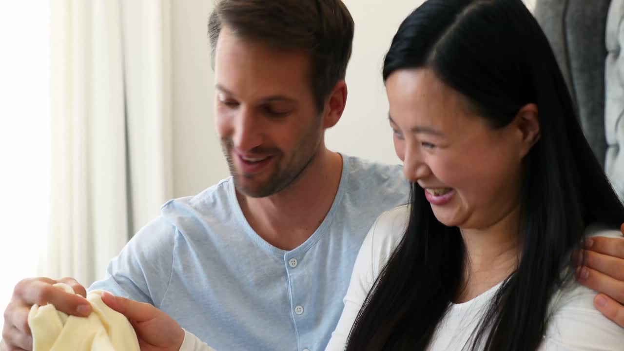 행복한 커플이 침실 4k에서 아기 옷을 확인합니다.