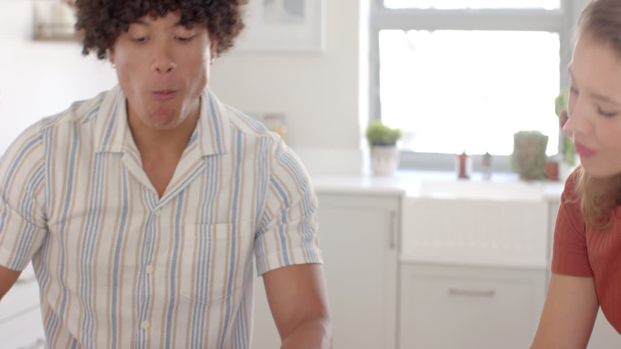 Young man holding coffee mug, talking with woman in bright kitchen, at home