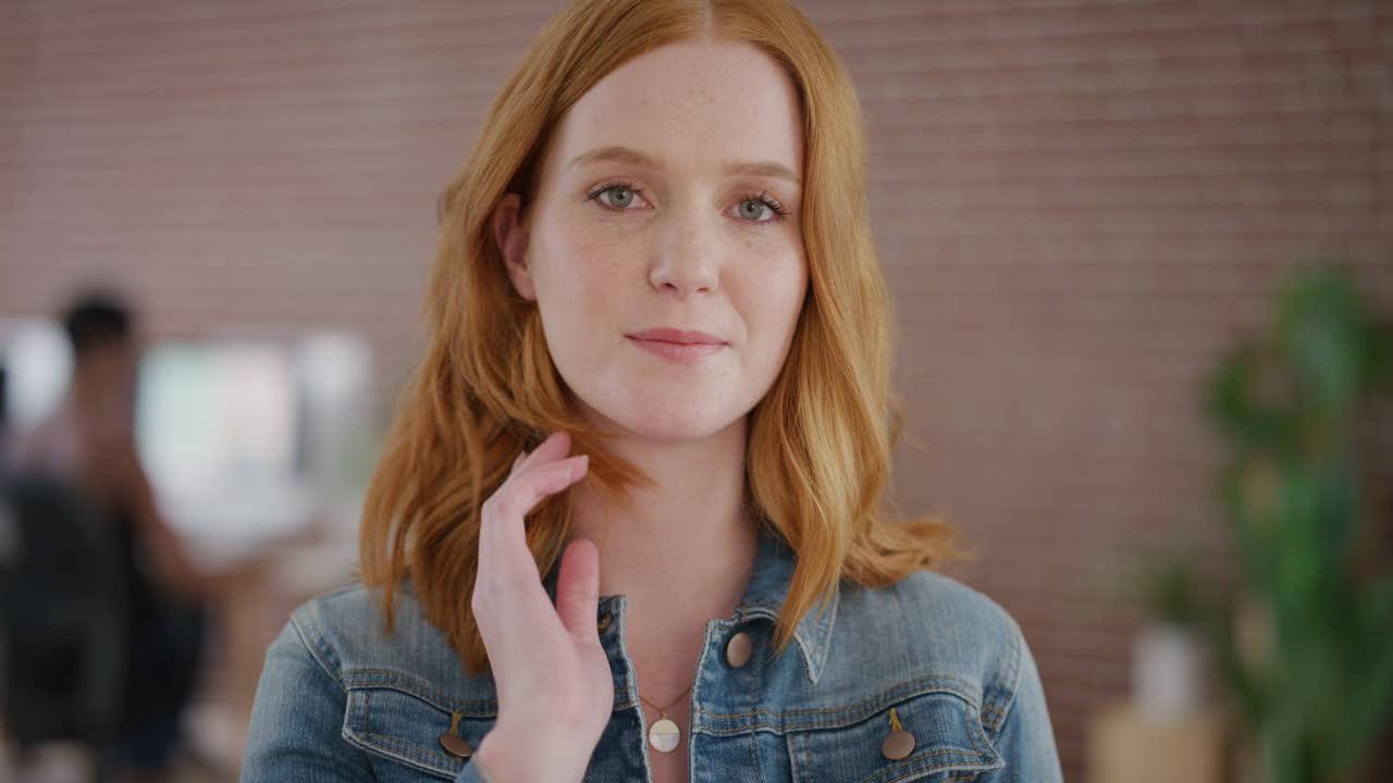 portrait beautiful red head woman intern smiling running hand through hair office workspace background