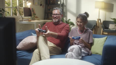 father and daughter playing video games together on a couch at home