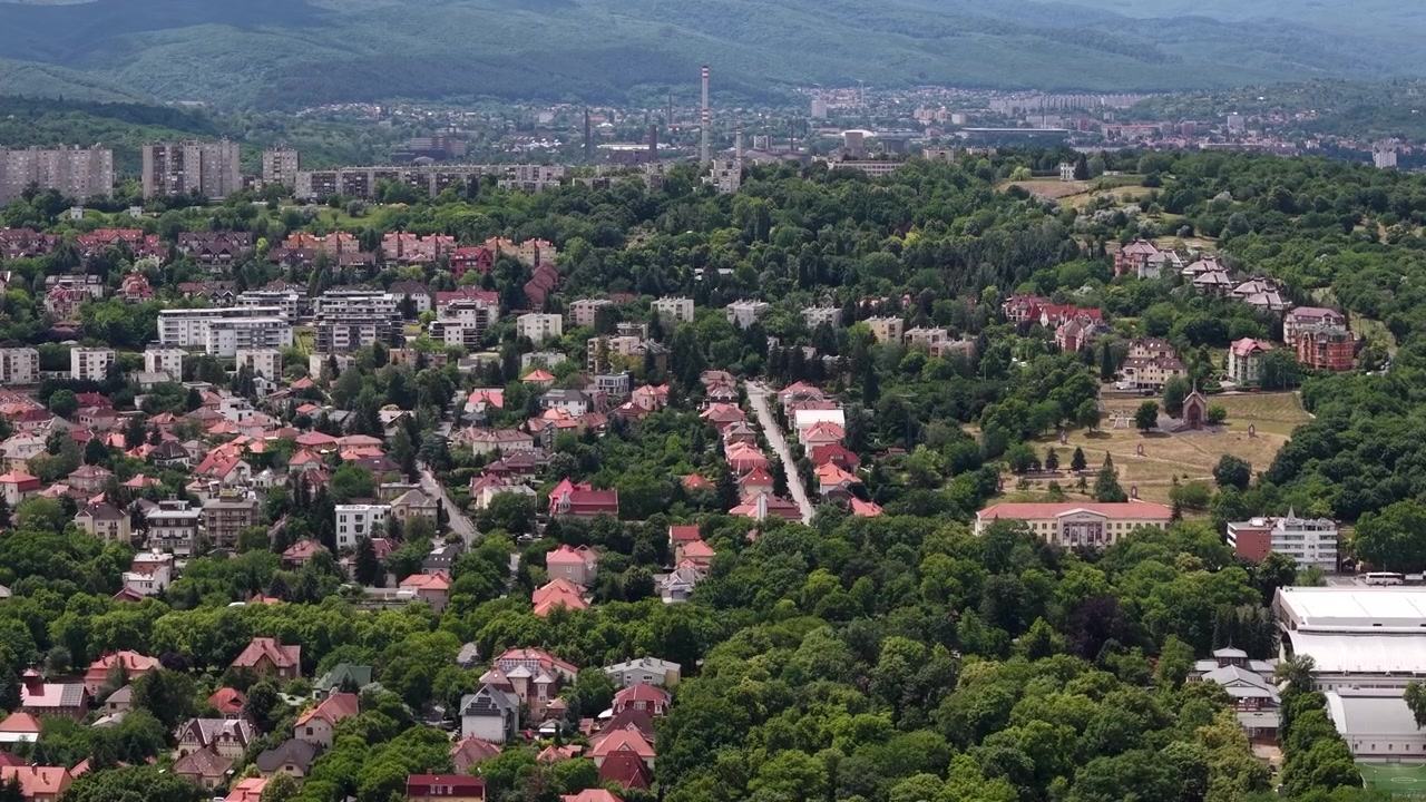 Uma vista de ângulo elevado da cidade húngara de Miskolc, mostrando uma densa área residencial cercada por colinas arborizadas de verde vibrante.