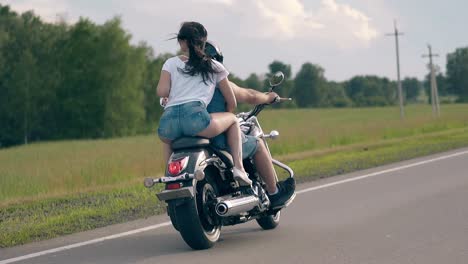 young couple in denim dressing rides motorcycle along road