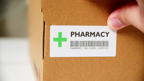 Hands-applying-+PHARMACY-Sticker-label-on-a-shipping-cardboard-box