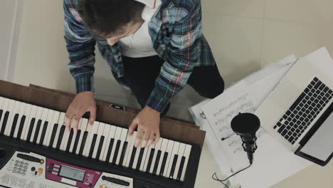 joven músico masculino cantando y tocando teclado eléctrico en casa