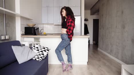 Attarctive-girl-in-red-flannel-shirt-doing-a-dance-off-in-her-loft-cozy-studio-apartment,-enjoying-her-free-time,-enjoying-youth.