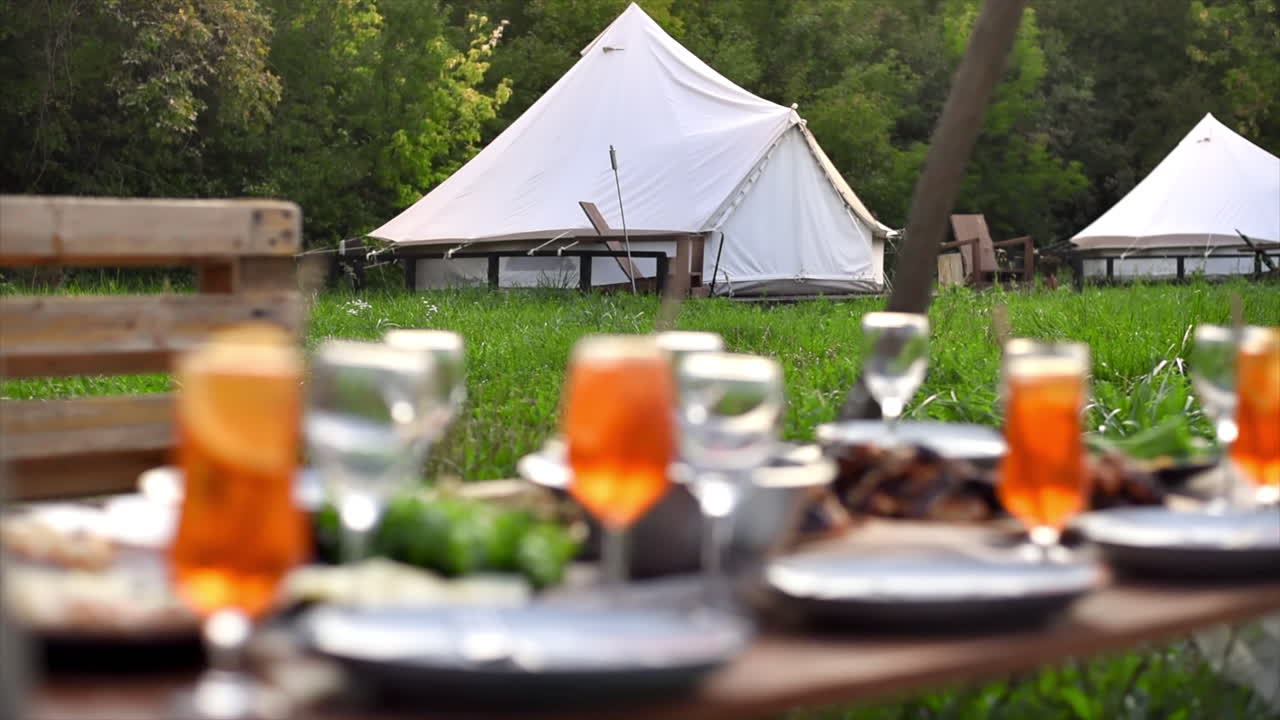Tavolo con cibo e bevande al glamping, vegetazione circostante, tende sullo sfondo