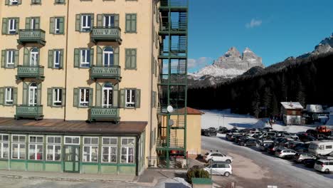 descending pedestal aerial shot of a large building with a frozen misurina lake and italy's three peaks of lavaredo in the distance