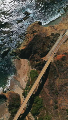view of the roads in the mountains connected by the bridge. rocky coastline of california with beautiful blue ocean from aerial perspective. vertical video